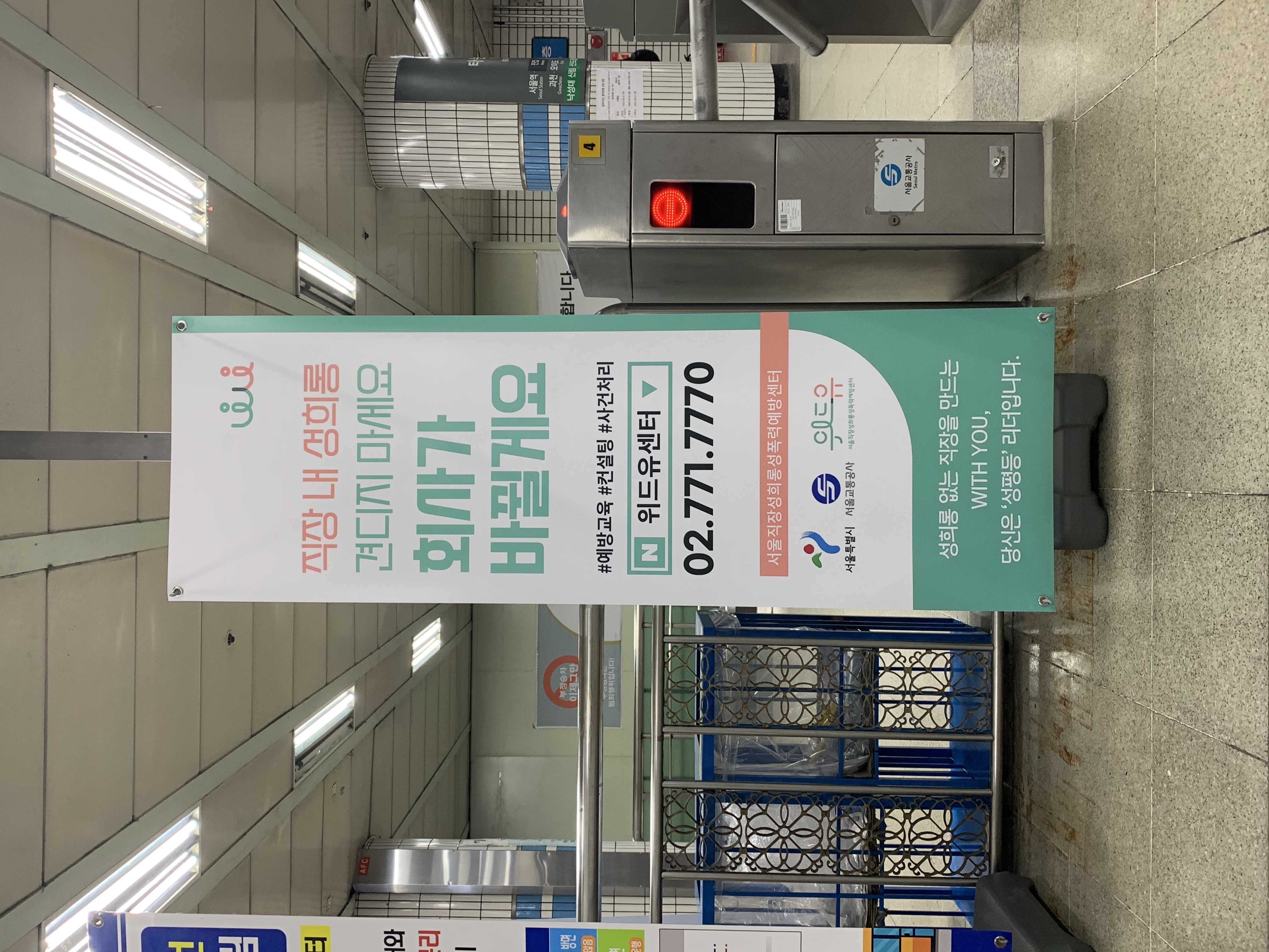 지하철 사당역 게이트 앞에 직장 내 성희롱 예방 배너가 설치된 사진. 배너 내용. 직장 내 성희롱 견디지 마세요. 회사가 바뀔게요. 예방교육, 컨설팅, 사건처리. 검색창에 위드유센터. 02. 771. 7770. 서울직장성희롱성폭력예방센터. 서울특별시. 서울교통공사. 위드유 서울직장성희롱성폭력예방센터 3자 로고. 성희롱 없는 직장을 만드는 WITH YOU 당신은 성평등 리더입니다. 끝.